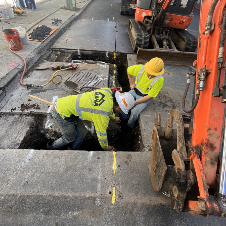 Mana crew working in an underground utility trench beside an excavator
